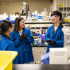 Four Temple Chemistry students wearing blue lab coats and talking together in a College of Science and Technology lab