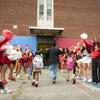 Two children being led into school while a crowd in Temple attire cheers